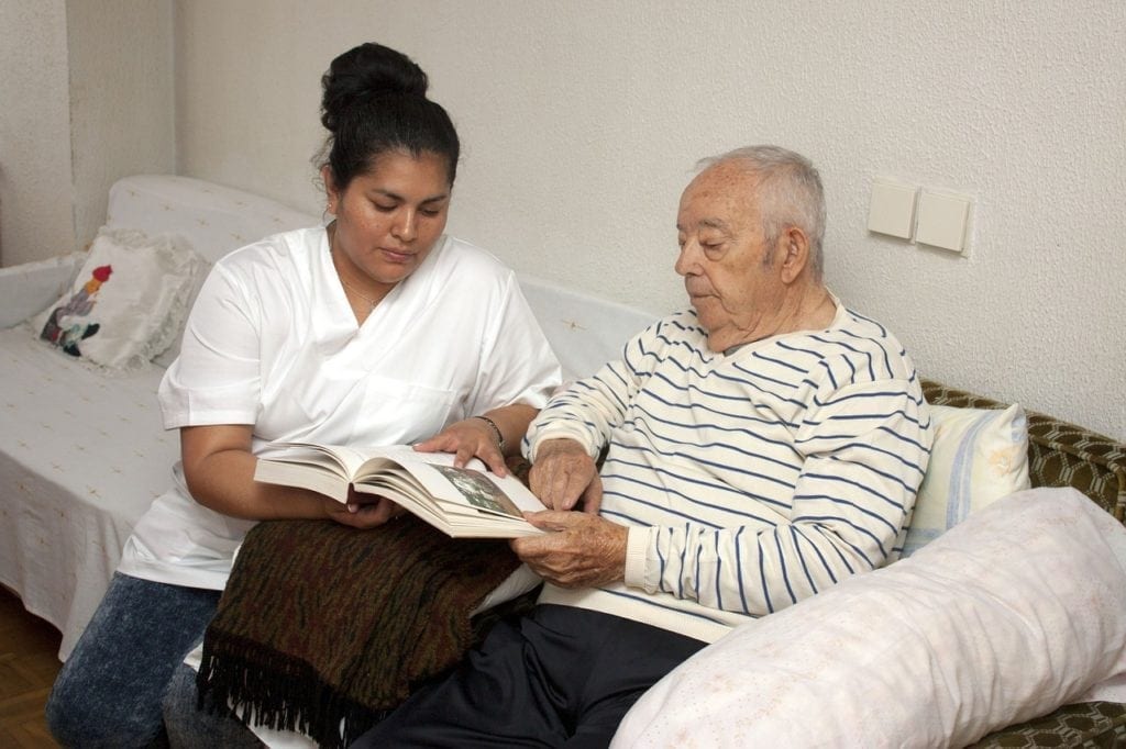 A nurse is helping an elderly man read.